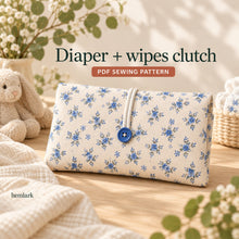 Closed ivory clutch with tiny blue flowers, a blue button and narrow ivory loop, styled on a wood table beside a knitted toy and flowers.