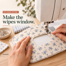 Hands topstitch around the rounded rectangular wipes opening in a flat blue floral pocket panel at a sewing machine.