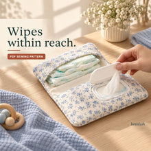 A hand lifts the white wipes-pack lid through a blue floral wallet pocket, with folded diapers in the opposite pocket.