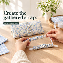 Hands thread elastic through a narrow blue floral fabric casing beside a finished clutch with a gathered strap.