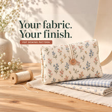 An ivory clutch with small pink and sage flowers and a wooden button stands on coordinating floral and blue gingham fabrics beside a thread spool.