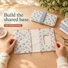 Hands clip a solid blue floral diaper pocket and a window pocket onto a flat ivory lining panel before stitching the outer edges.