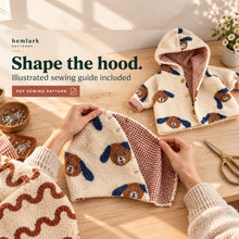 Hands align and pin hood fabric layers on a sewing table beside a completed lined sample. Cream dog-print sherpa and rust gingham.