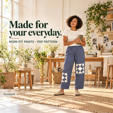 An adult model wears slate-blue relaxed elastic-waist pants with offset ivory quilt-star patches in a light-filled creative studio. Mom-Fit Pants PDF pattern.