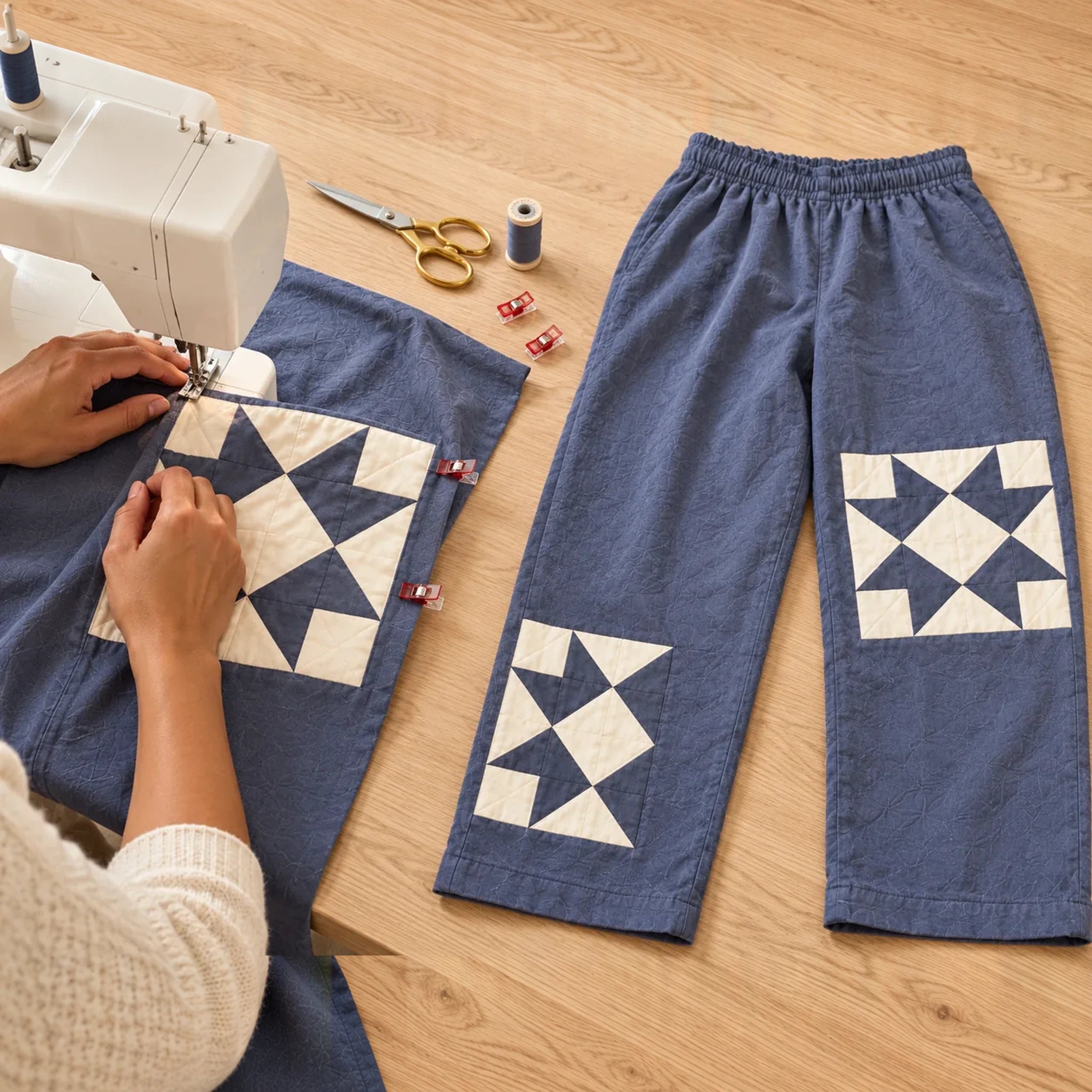 Slate-blue pants sewing project with quilt-star details and sewing tools